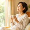 介護の不公平感から解放された50代女性が窓辺でお茶を飲んでいる様子