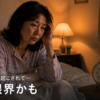 夜中に目が覚めた50代女性が疲れた表情でベッドに座っている。認知症介護による睡眠不足のイメージ。